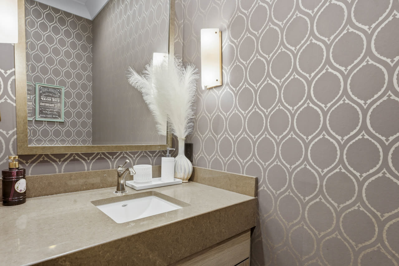 A powder room with grey patterned wallpaper and a stone vanity.