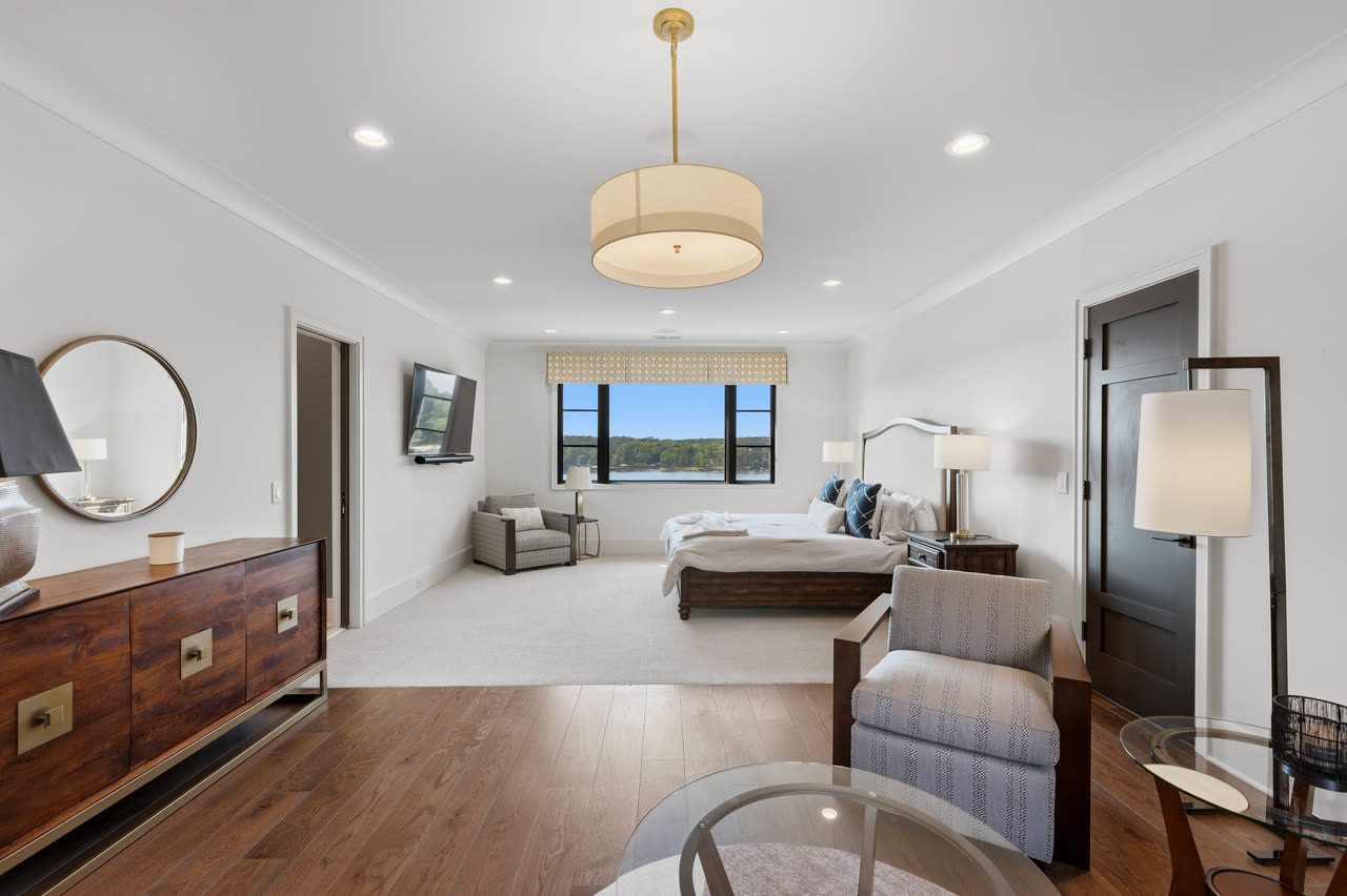 A guest bedroom with a dresser, sitting chairs and a lake window.