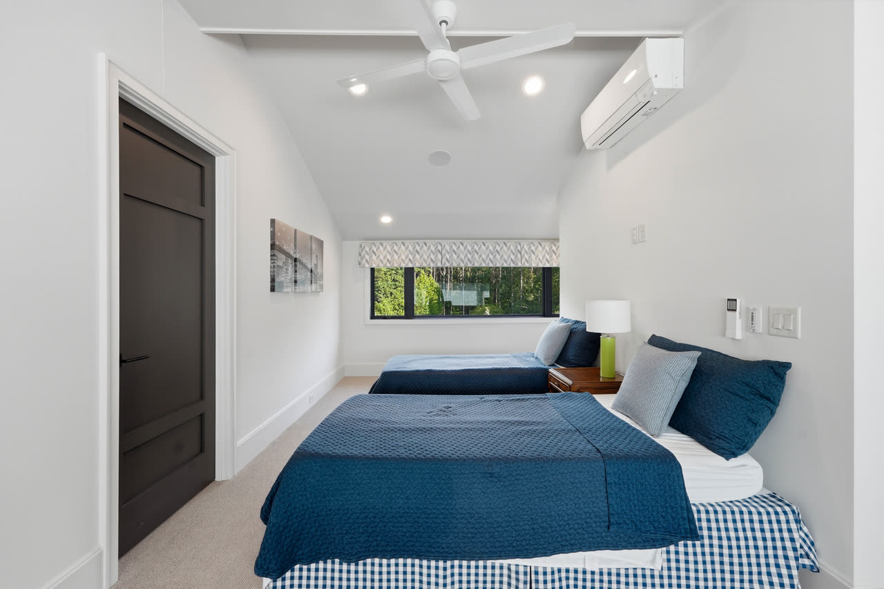 A guest bedroom with two beds in blue and a window to the trees.