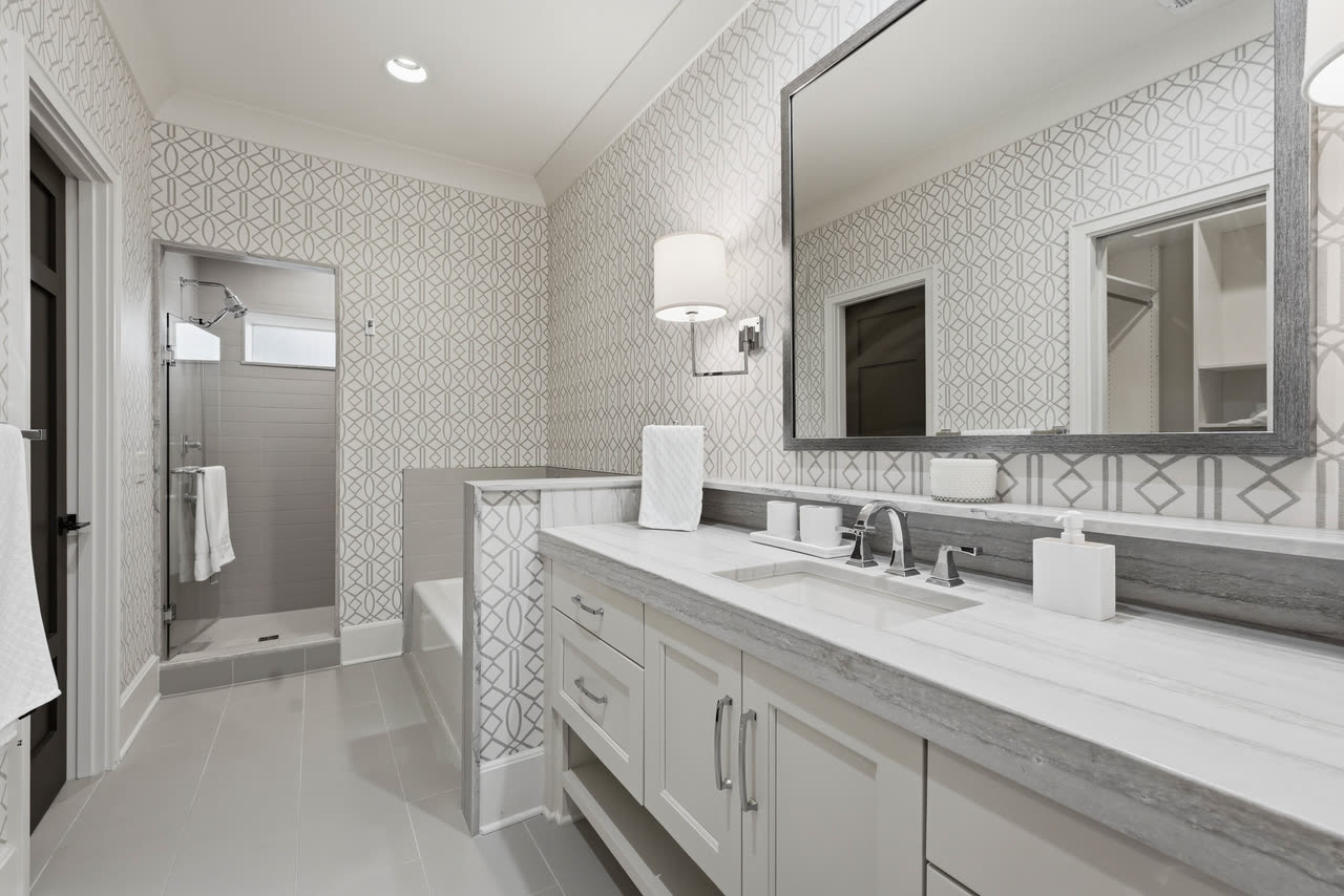 A guest bathroom with patterned wallpaper, a long vanity and a shower.
