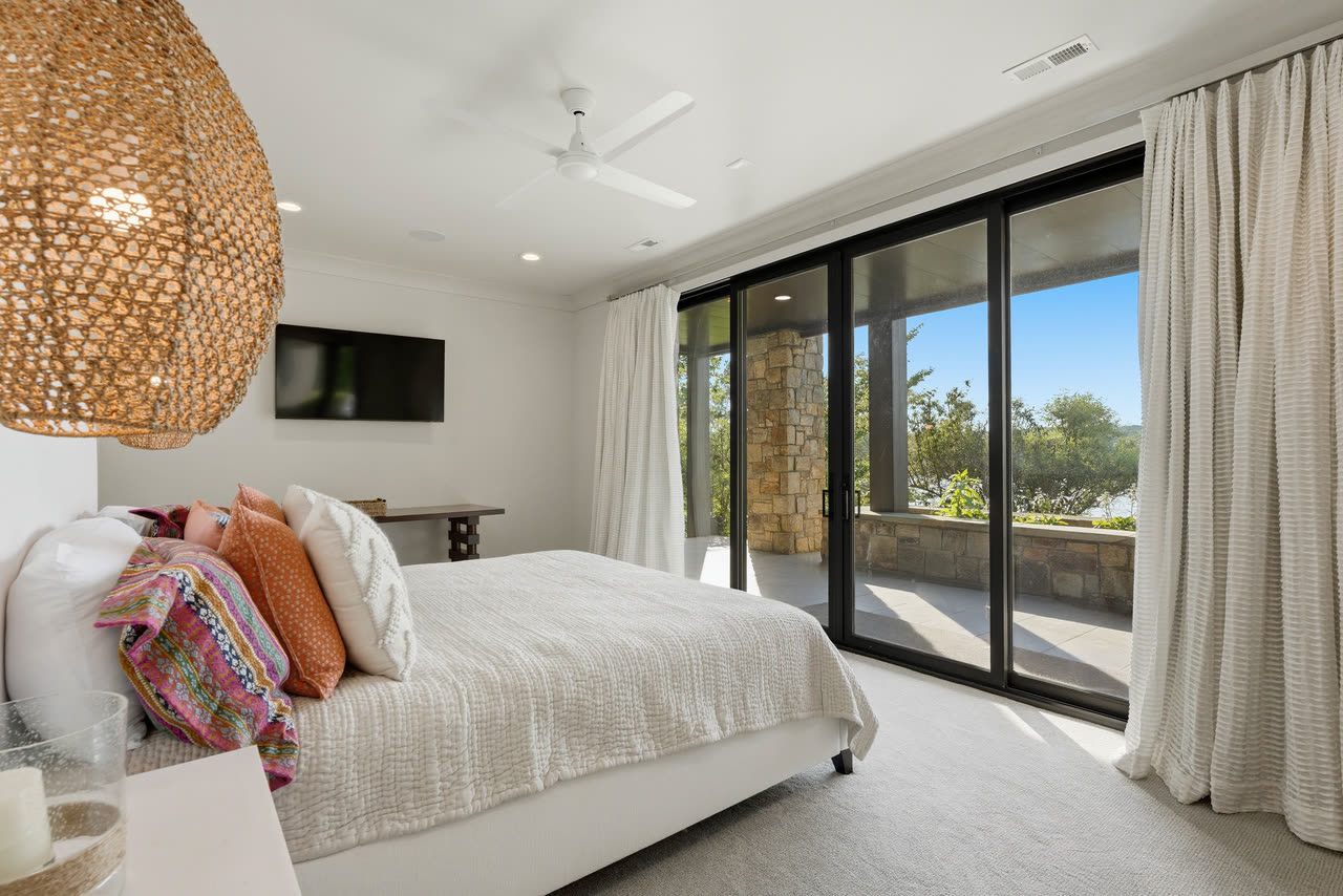 A guest bedroom under a woven pendant, doors open to the stone terrace.